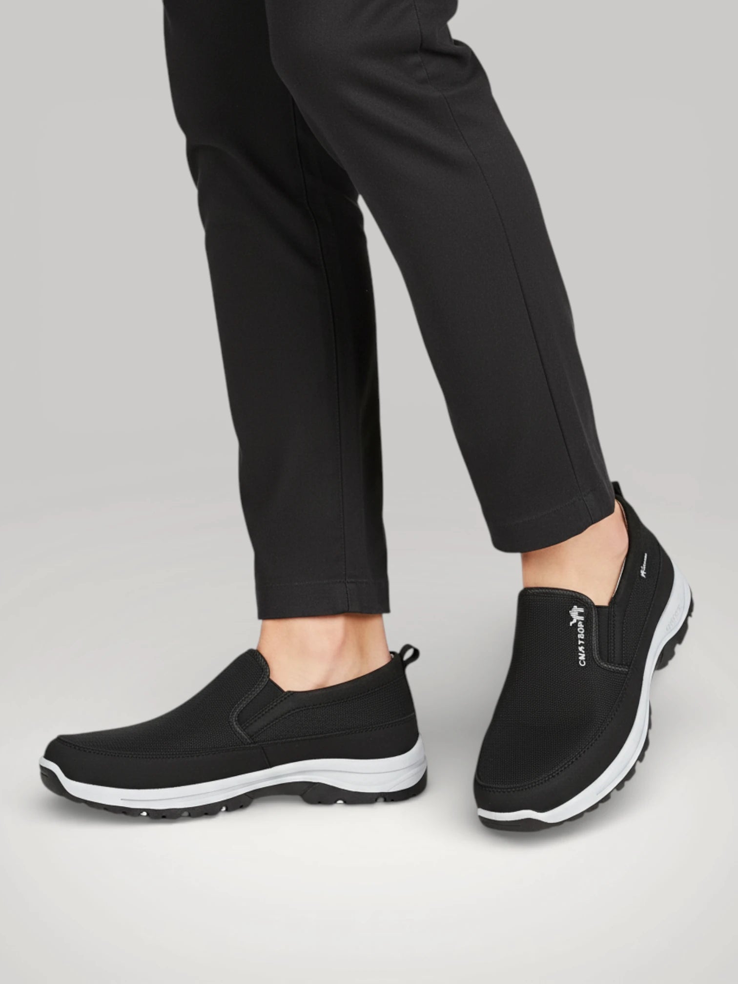 Chaussures de marche ergonomiques noires portées, offrant un soutien de la voûte plantaire et un confort quotidien - Urbain Couture.