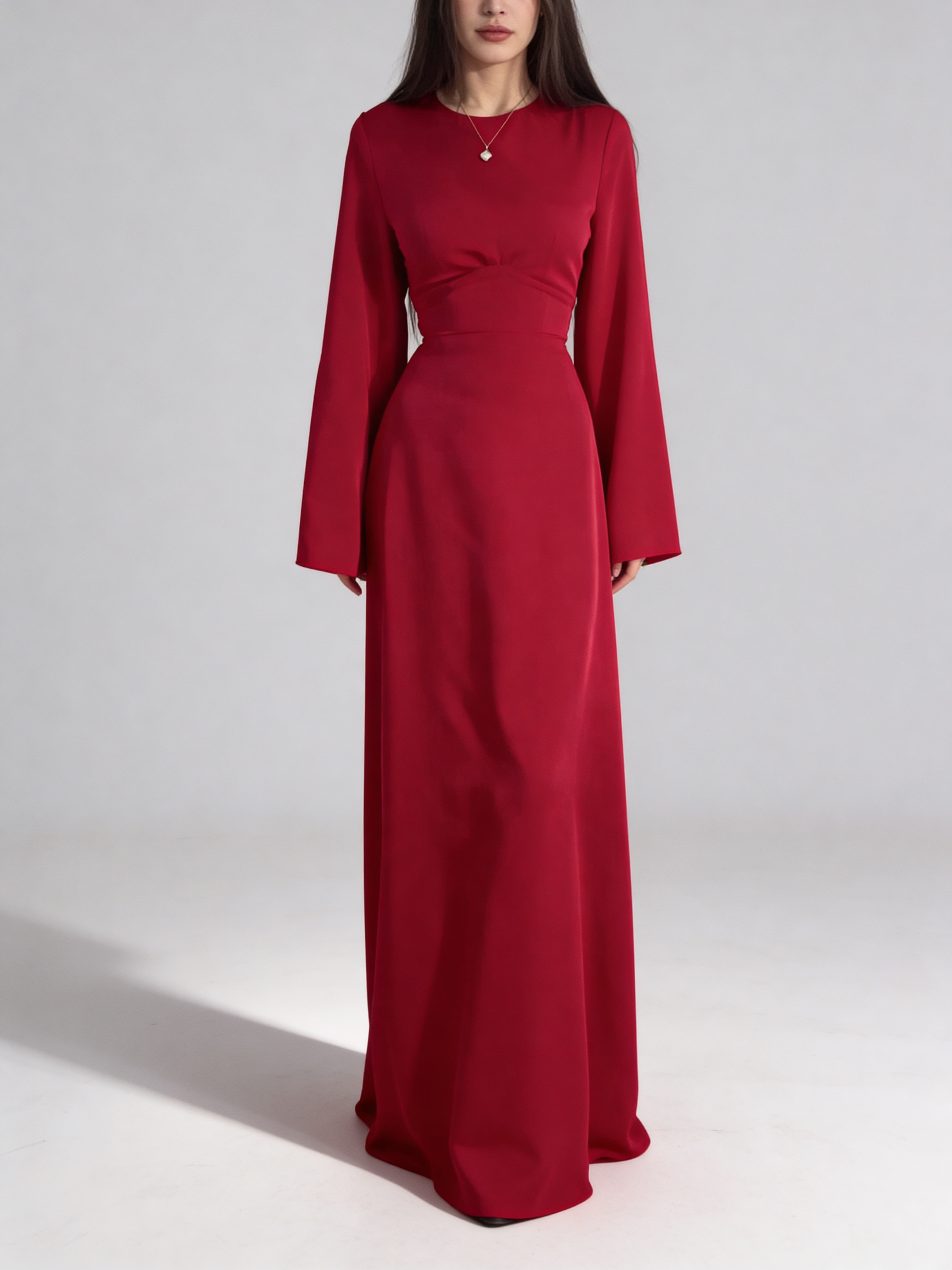 Femme portant la robe longue fluide en satin rouge, coupe cintrée à la taille et manches longues.