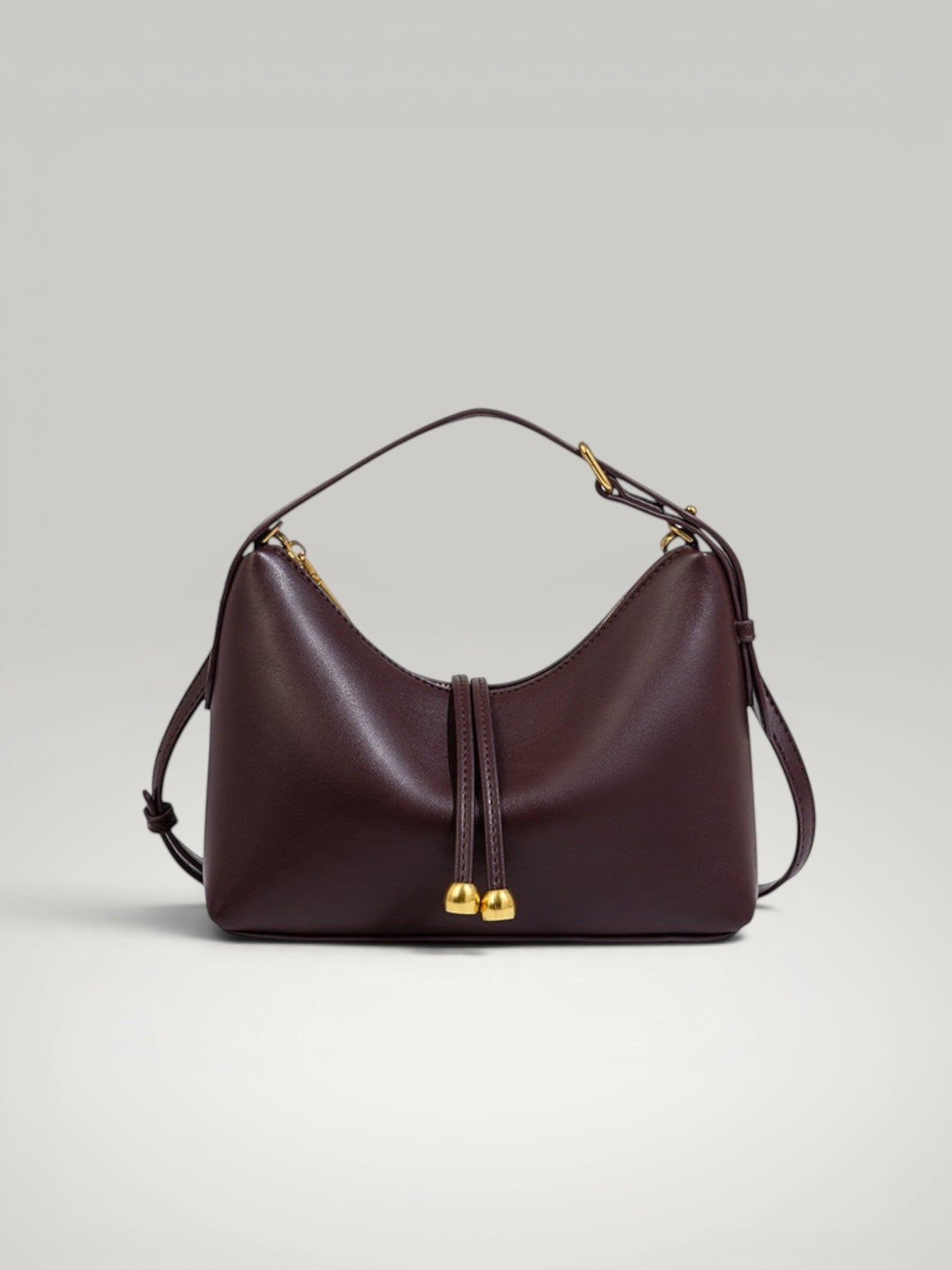 Sac à main élégant couleur bordeaux brique en cuir avec finitions métalliques dorées.
