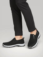Chaussures de marche ergonomiques noires portées, offrant un soutien de la voûte plantaire et un confort quotidien - Urbain Couture.