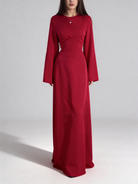 Femme portant la robe longue fluide en satin rouge, coupe cintrée à la taille et manches longues.