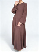 Femme portant une robe longue fluide couleur moka royal avec des manches larges évasées, style modeste en tissu texturé.