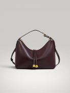 Sac à main élégant couleur bordeaux brique en cuir avec finitions métalliques dorées.
