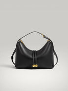 Vue de face du sac à main Lune en cuir noir avec boucles dorées sur fond gris clair.