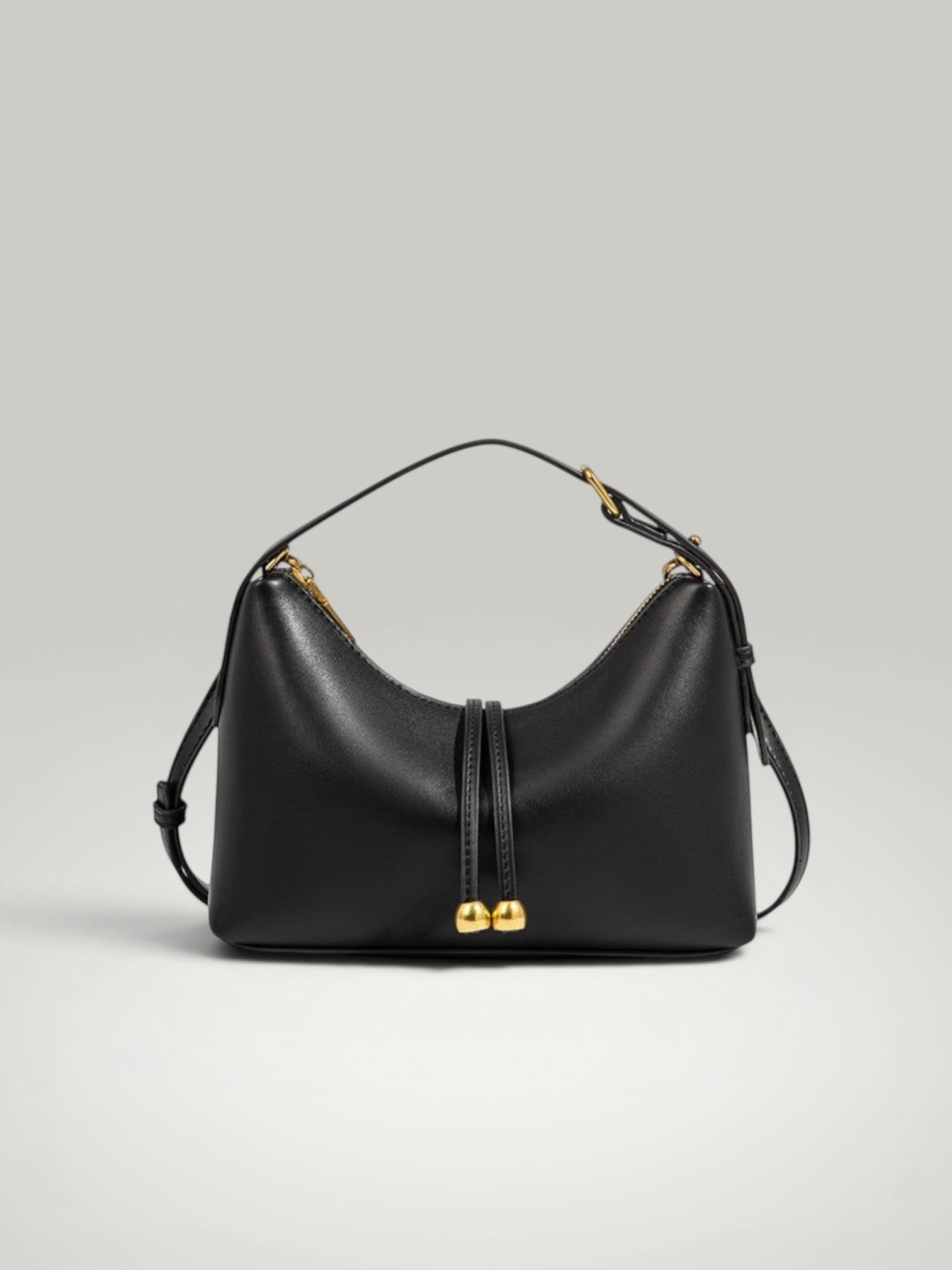 Vue de face du sac à main Lune en cuir noir avec boucles dorées sur fond gris clair.